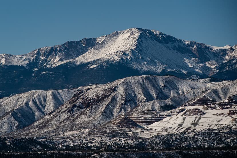 A snow-capped mountain peak rises above a rocky landscape under a clear sky.