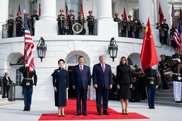 Donald Trump and Xi Jinping stand together during a White House ceremony with American and Chinese flags.