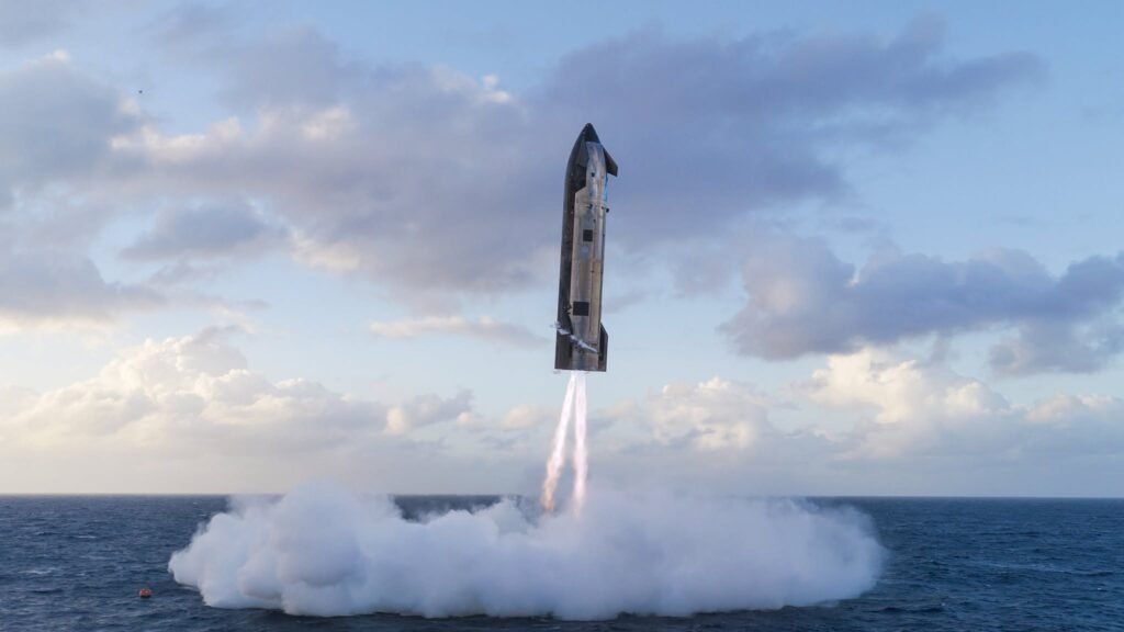 A rocket booster descends toward ocean water with flames visible at its base.