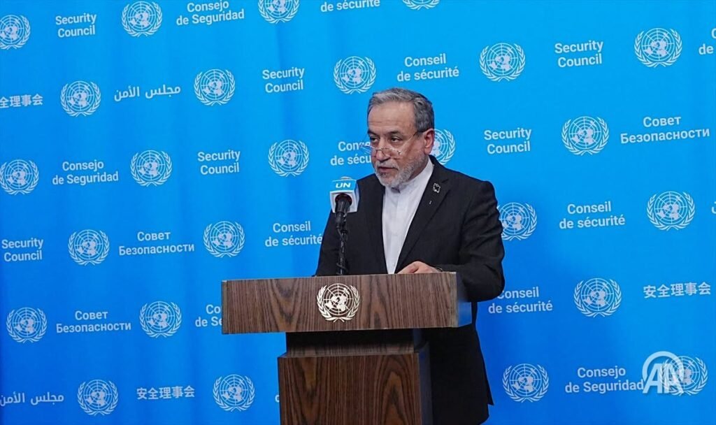 A man in a dark suit speaking at a podium with microphones in front of him.