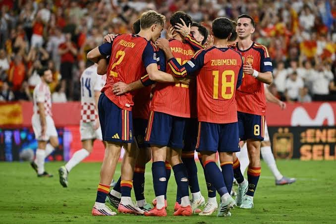 A group of soccer players in red jerseys celebrate together on the pitch.