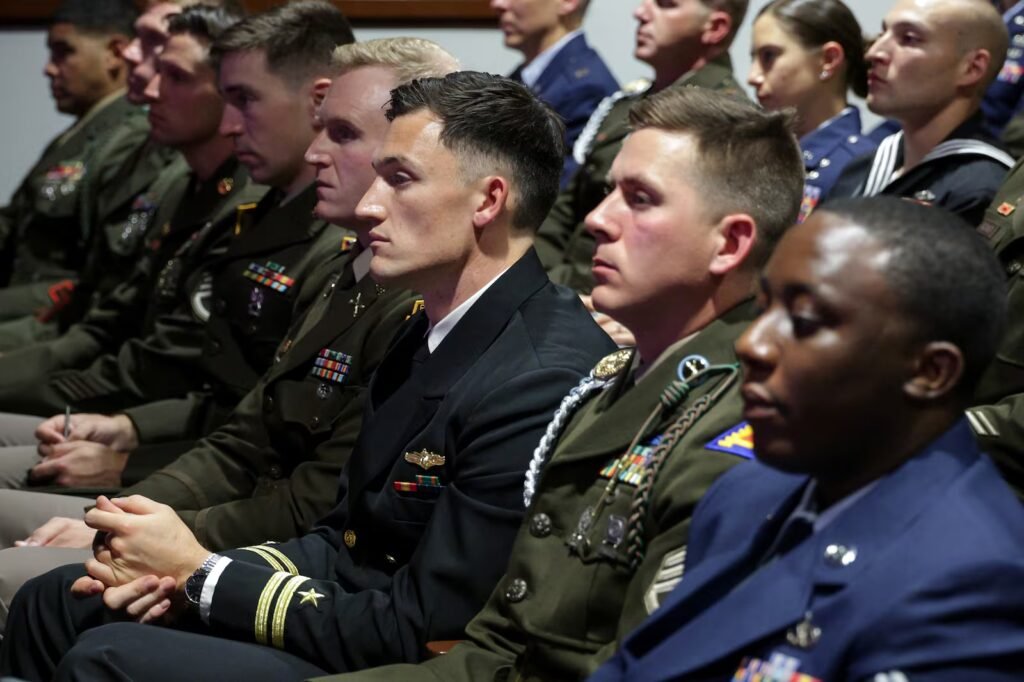 Rows of uniformed military personnel seated in an auditorium during a speech.