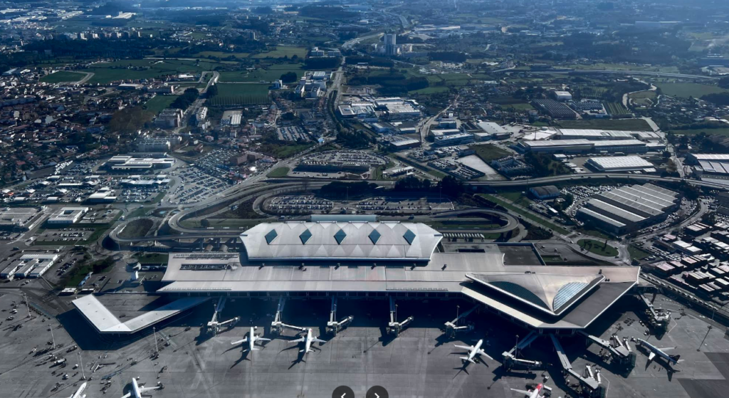 The exterior of an airport terminal building in Portugal with a road and vehicles in front.