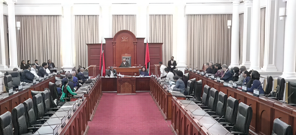 An ornate legislative chamber with rows of seats facing a central presiding desk.