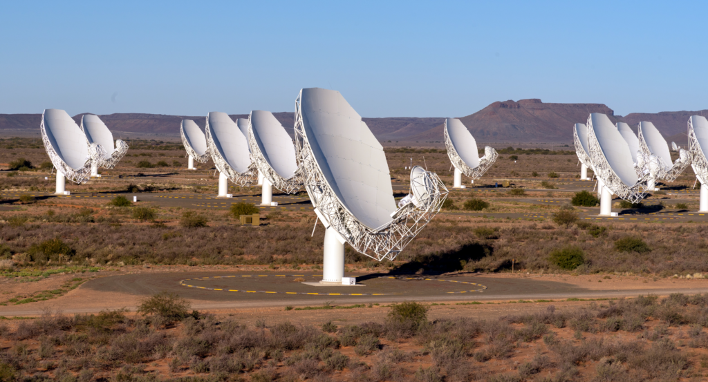 Multiple large white satellite dish antennas arranged across an open field under a clear sky.