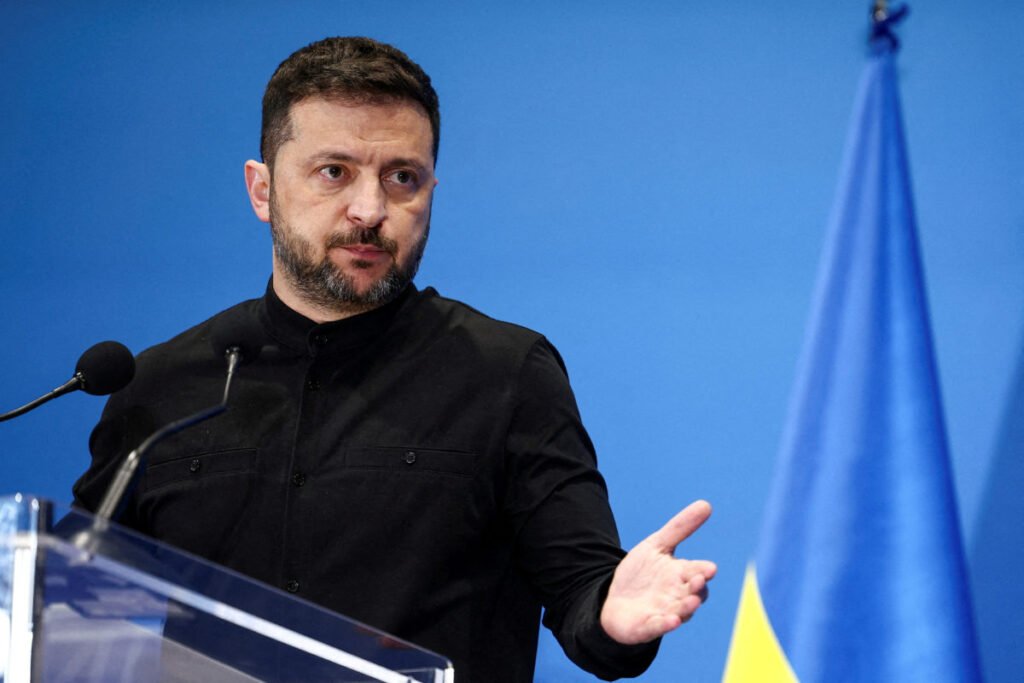 Volodymyr Zelenskyy speaking at a podium in front of Ukrainian flags.