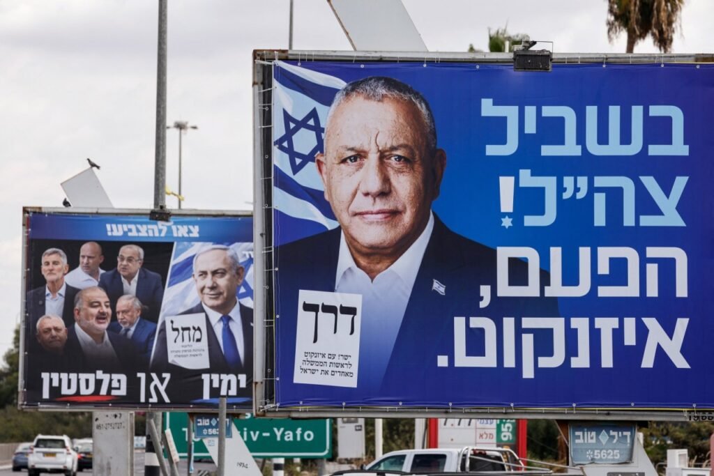 A large billboard with two men’s portraits beside a road sign.
