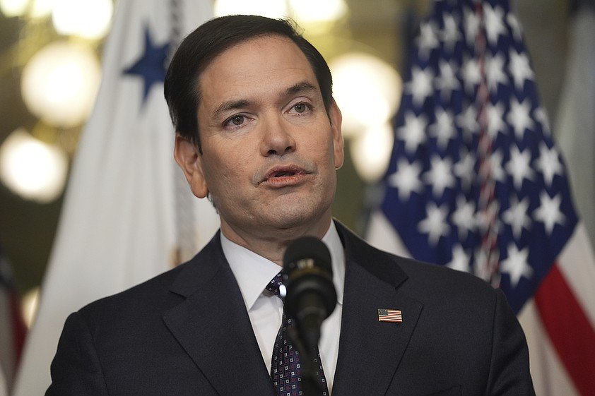 A man in a suit speaking at a podium in front of a flag.
