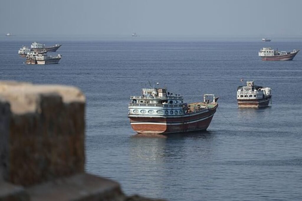 Tankers and cargo vessels at sea in the Strait of Hormuz under a hazy sky.