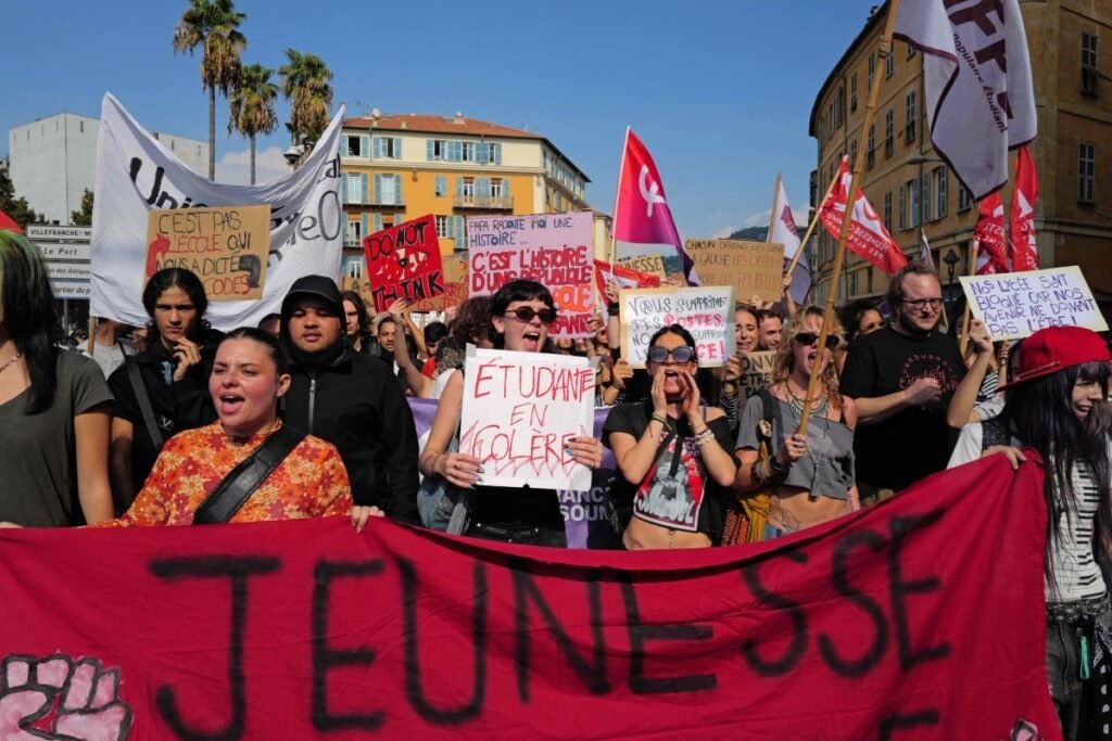 A crowd of young demonstrators marches through a city street holding signs.