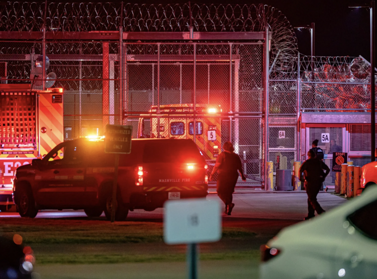 Emergency vehicles with flashing lights are parked outside a correctional facility at night.