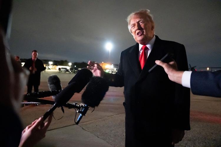 A man in a dark suit speaking to reporters on an airport tarmac.