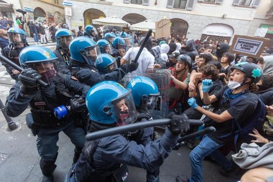 Police in riot gear facing a group of protesters on a street in Milan.