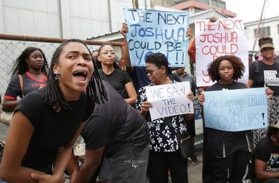A crowd of protesters holding signs on a street in Trinidad.