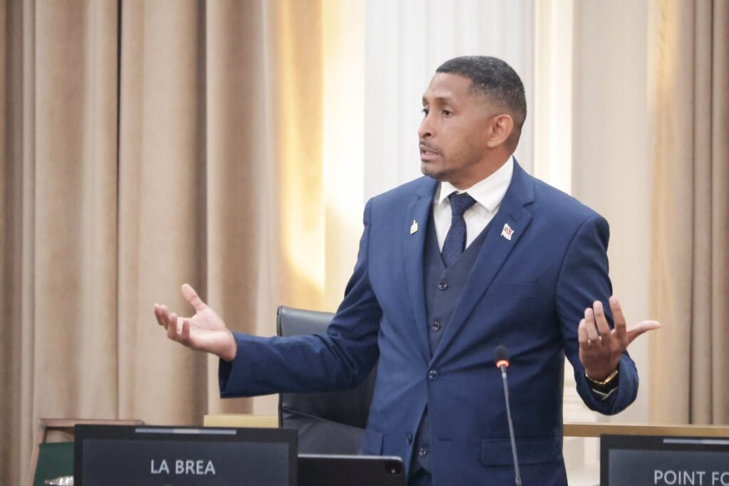 : Minister Clyde Elder in a suit speaking at a podium.