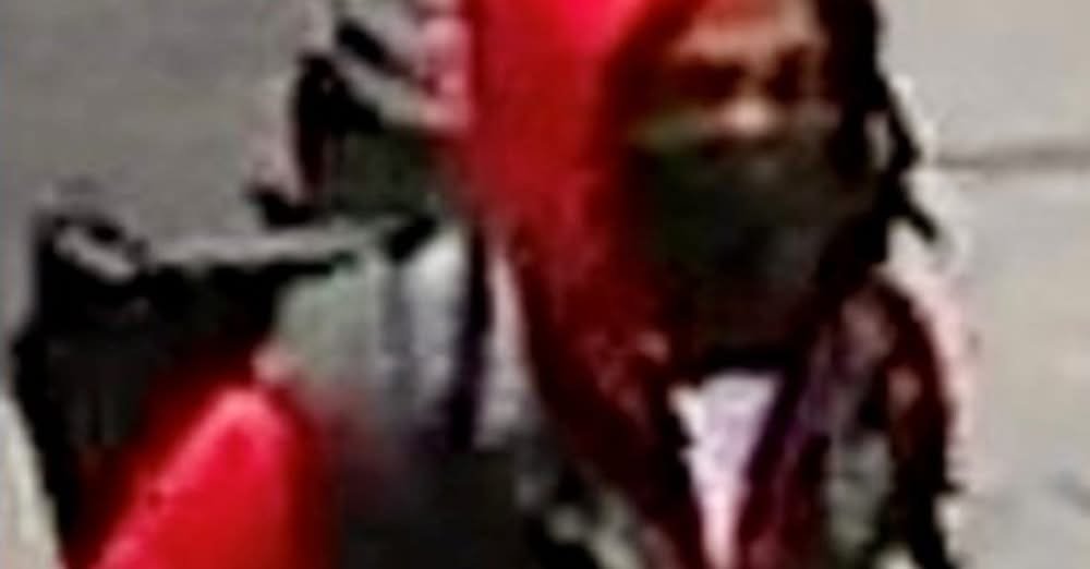 A security camera image of a person in a red tracksuit, black vest and black face mask carrying a backpack.