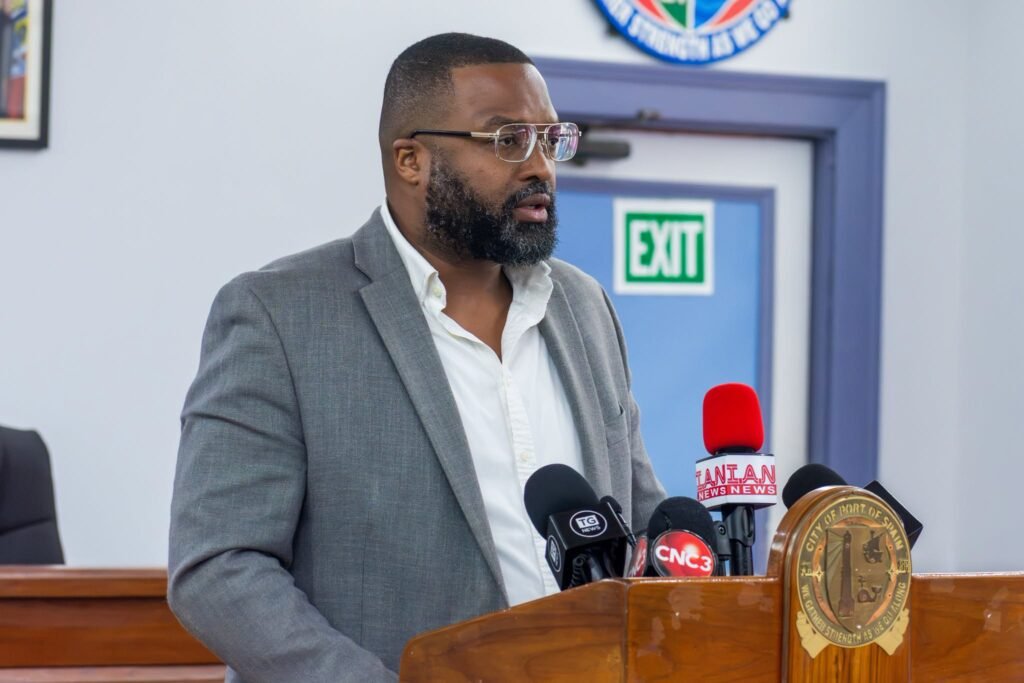 A man in formal attire speaks at a podium inside a government building.