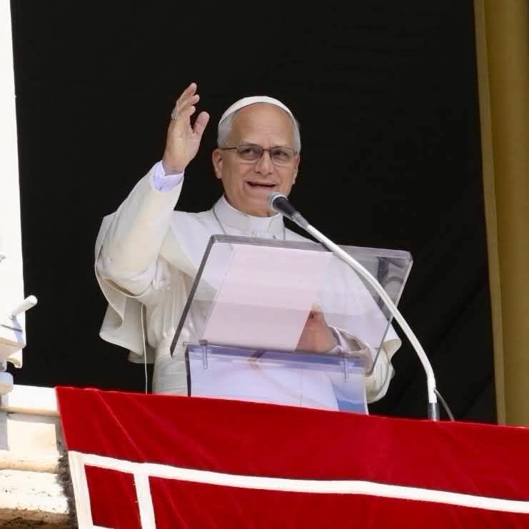 A man in white papal vestments speaking from a window above a crowd in St. Peter’s Square.