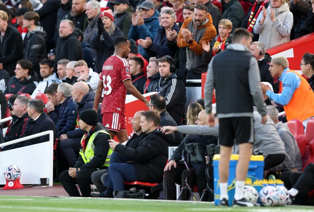 A Liverpool player in a red shirt walking off the pitch past a referee.