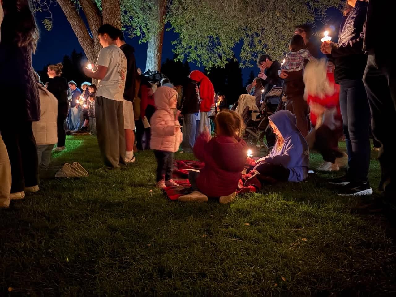A group of people stand together outdoors at night holding candles.