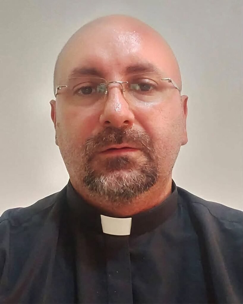A priest wearing glasses and a black clerical shirt.
