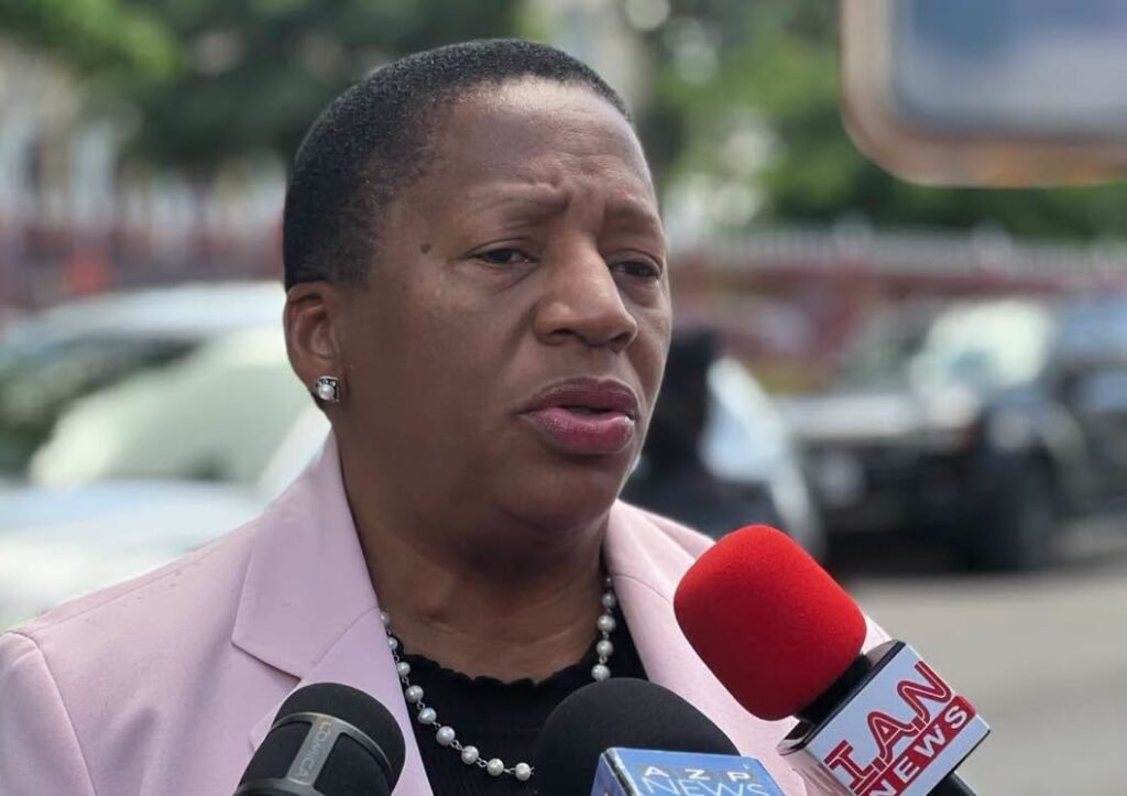A woman in a business suit speaking to reporters outside a government building.