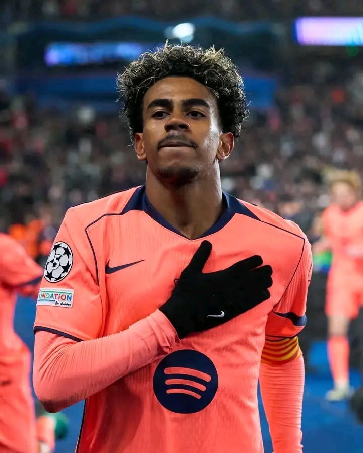 A young soccer player in a Barcelona kit running with his arm raised.