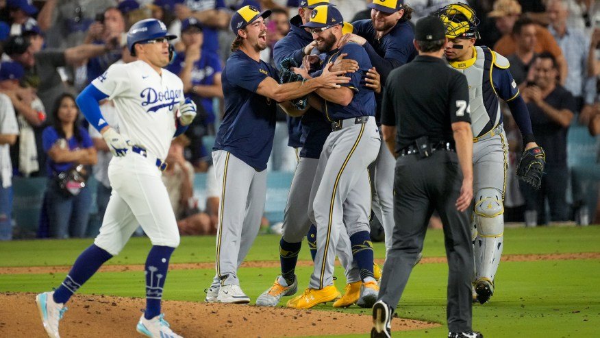 Baseball players in gray uniforms hugging and jumping together on the infield after winning a playoff series.