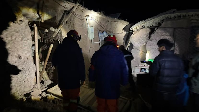 Firefighters in uniform walking past damaged stone houses in a Tibetan village.