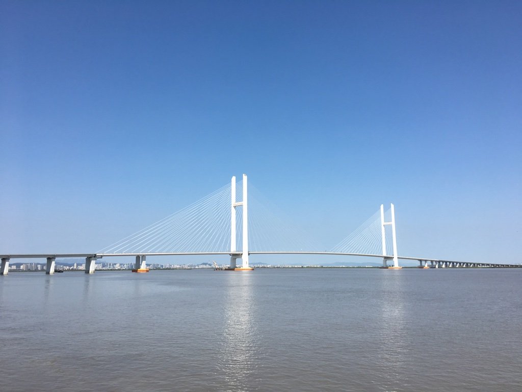 A long road bridge crossing a wide river between two cities.