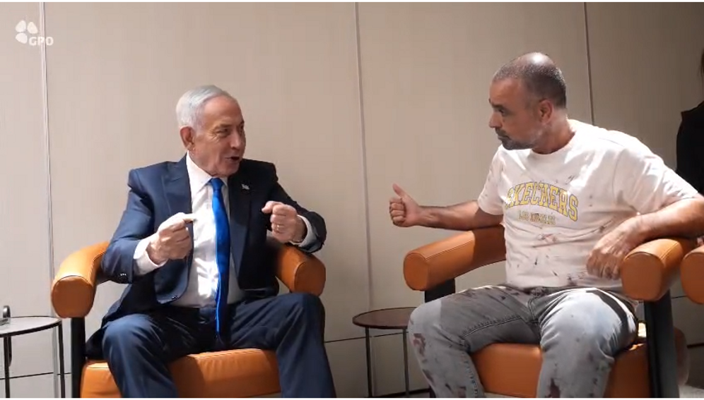 Two men speak together indoors.