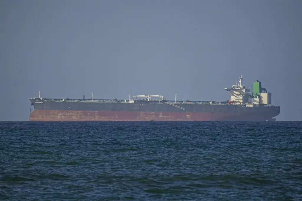 A large tanker ship travels through a narrow strait with coastline visible in the distance.