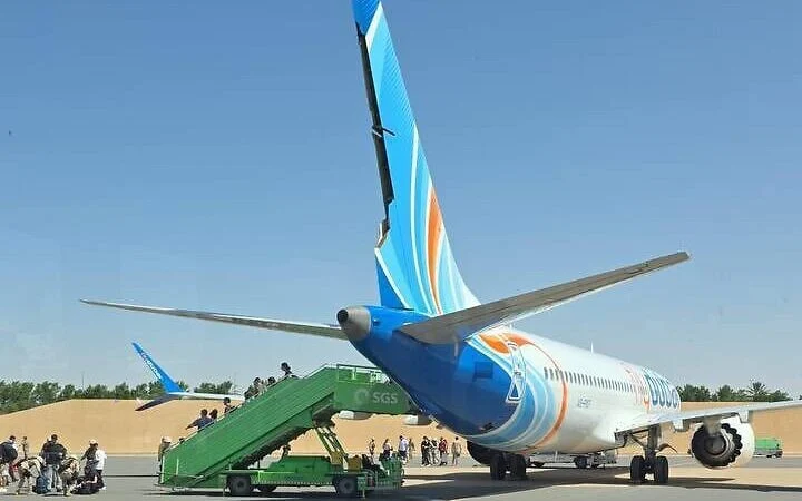 A white passenger jet with orange tail markings sits on an airport tarmac.