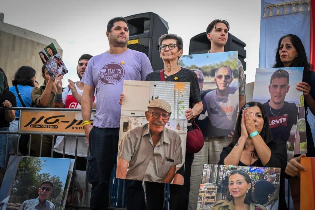 A group of people hold large cardboard cutouts of faces as they stand outdoors near a government building in Jerusalem.