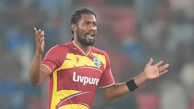 A bowler in a maroon uniform celebrates with his arms raised during a night match.