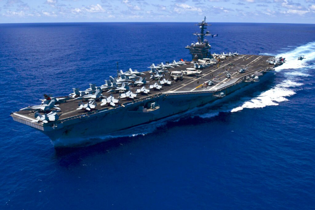 An aircraft carrier with jets on its flight deck at sea.