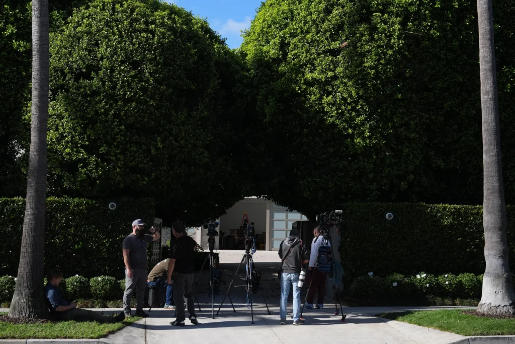 A large house behind a hedge with law enforcement vehicles outside.