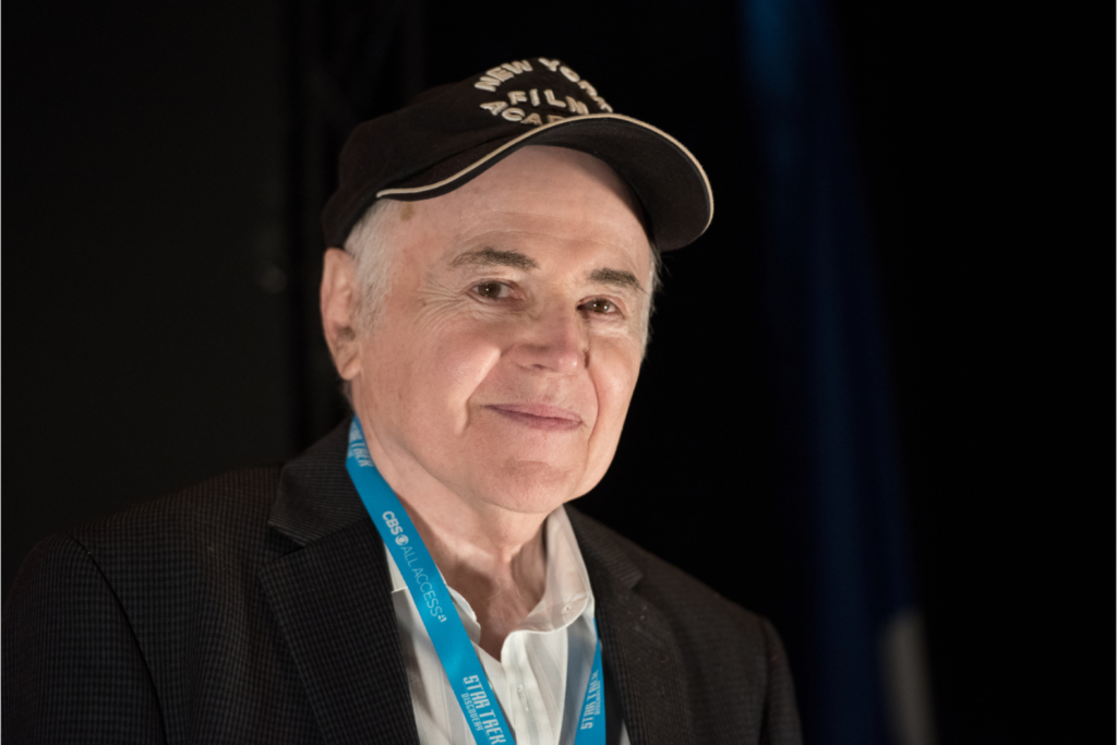 An older man smiling at a fan convention.