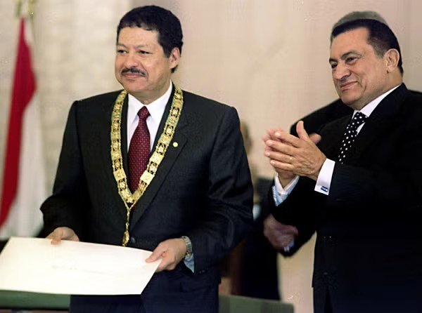 A smiling older man in a dark suit at an award ceremony.