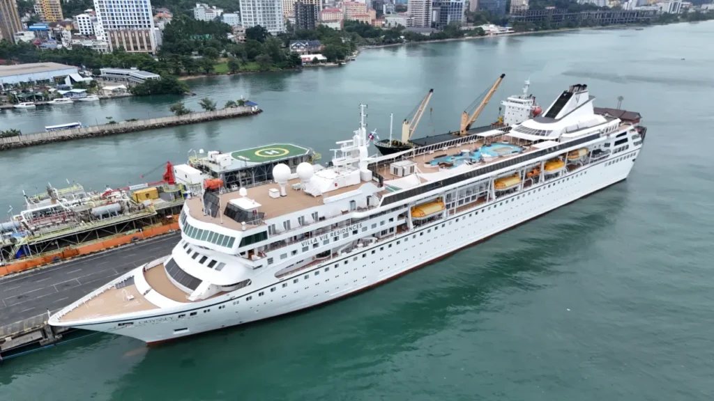 A cruise ship at anchor near a tropical coastline.
