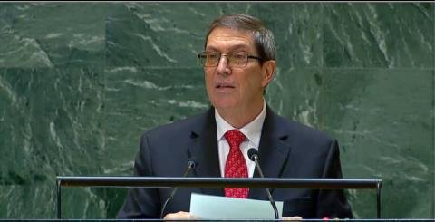 A man in a dark suit speaking at the General Assembly podium with a green backdrop.