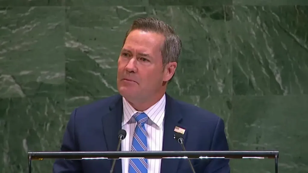 A man in a dark suit speaking at the General Assembly podium.
