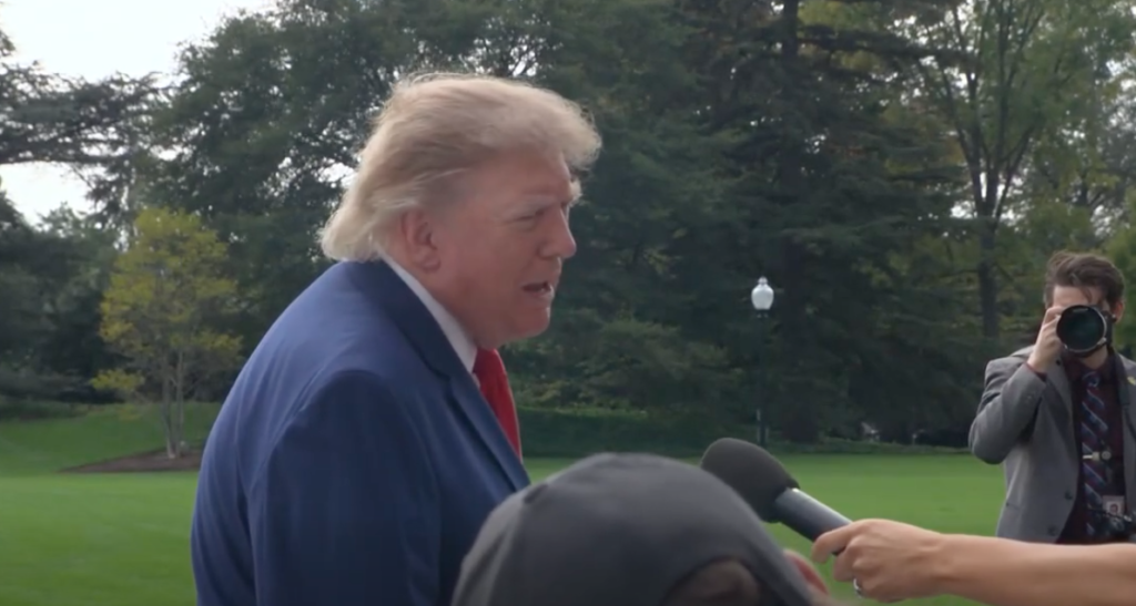 A man in a dark suit speaking to reporters on the White House grounds.