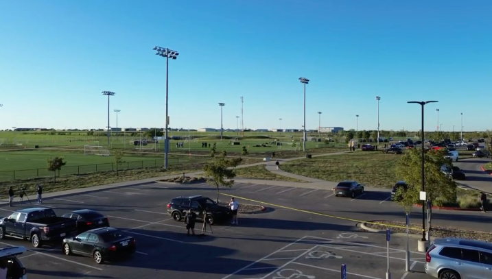Emergency workers standing near parked emergency vehicles beside a sports field.