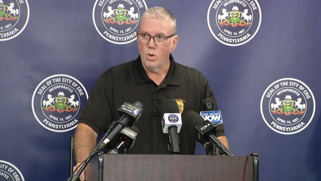 A uniformed police chief speaking at a podium in front of microphones.