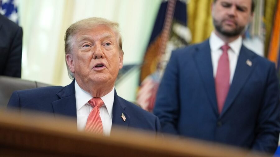 Donald Trump seated at the Resolute Desk speaking to reporters.