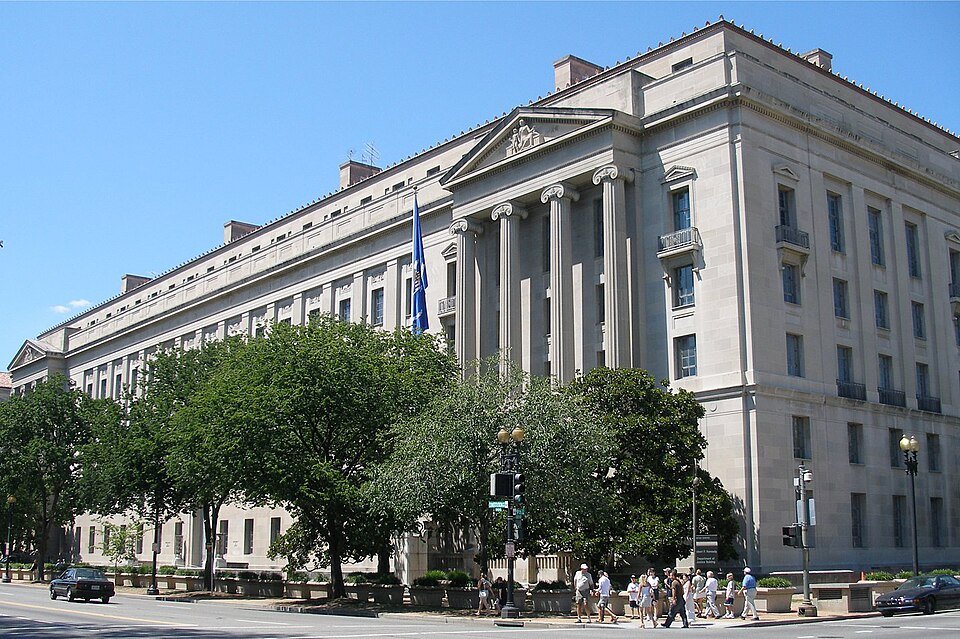 Front of the Department of Justice headquarters in Washington, a large stone government building with flags along its entrance.