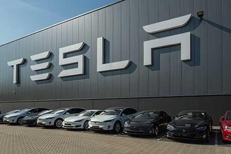 A row of electric vehicles parked outside a factory.
