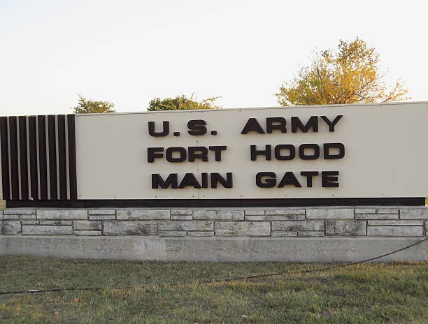 A large sign stands at the entrance to a military base beside a road.