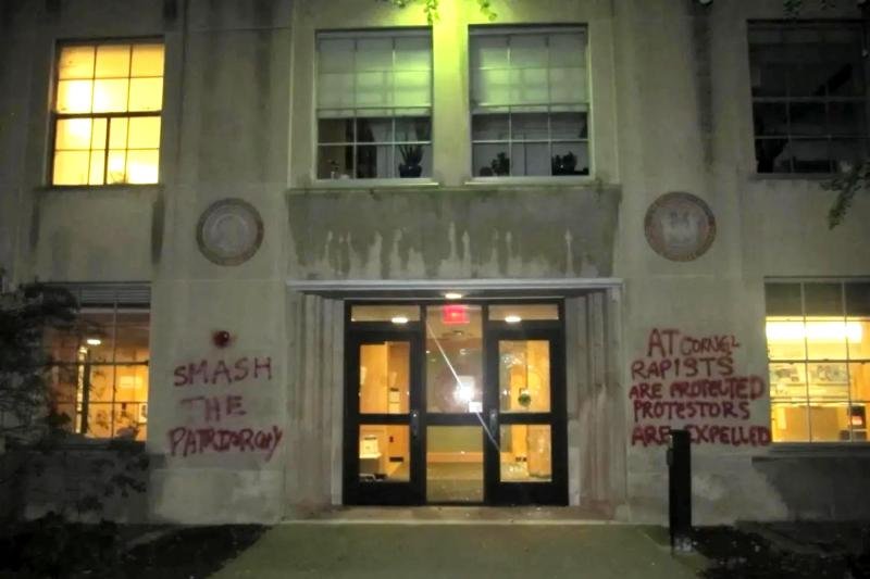 A building entrance shows a shattered glass door and spray-painted messages on the walls.